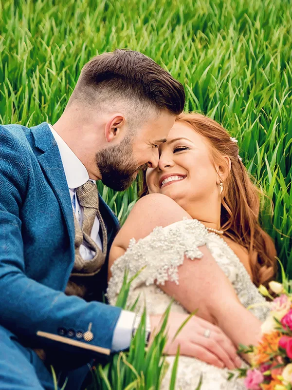 Groom and bride laying down in a field surrounded by tall grass in Worcester