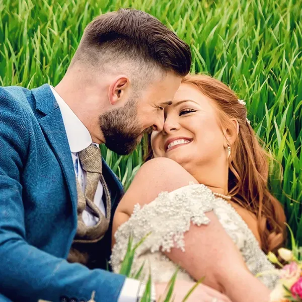 Groom and bride laying down in a field surrounded by tall grass in Worcester