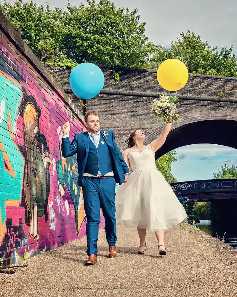 Newlyweds enjoying a playful walk with balloons along the water in Daventry