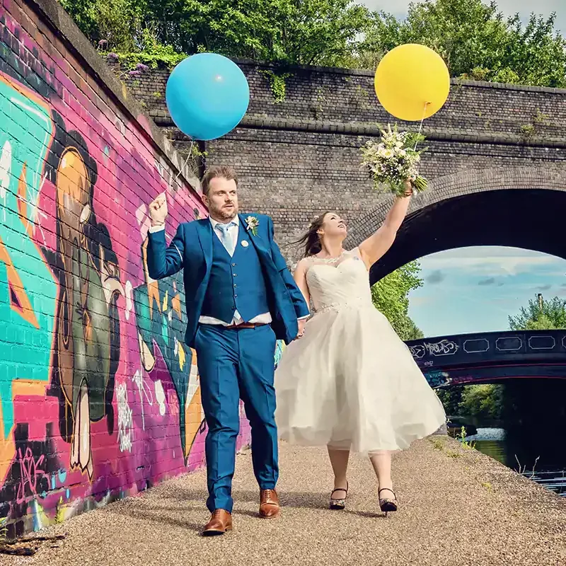 Newlyweds holding balloons walking along Worcester canal